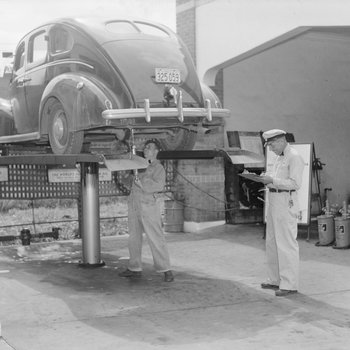 Two men inside of a Gulf Service Station shop inspecting and working on a car.