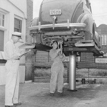 Two men inside of a Gulf Service Station shop inspecting and working on a car, vertical view.