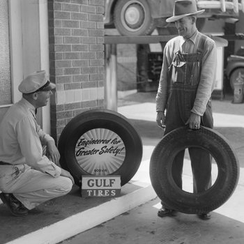 Two men talking at a Gulf Service Station next to a Gulf tire display.