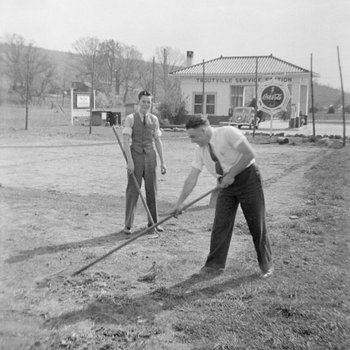 Two men working in a field in front of the Troutville Service Station.