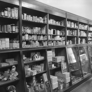 Inside of Everly Drug Store, view of wall shelves containing stuffed animals, feminine products, various medicines, etc.
