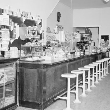 Inside of Dominion Lunch Restaurant, view of counter and bar stools, with various food items for sale behind the counter. New Market, Va.