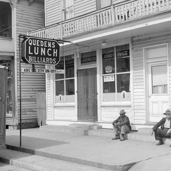 Quedens Lunch Billiards, New Market, Va. Alternate view from the street, with two men sitting on the sidewalk in front.