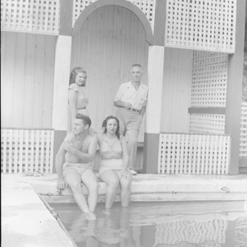 Four people sitting and standing on the edge of the swimming pool at the Shenandoah Alum Springs Hotel. Orkney Springs, Va.