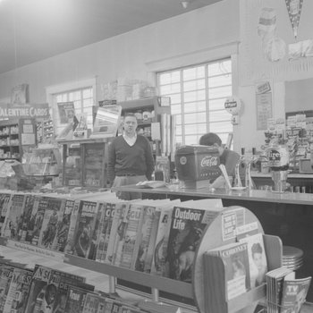Alternate view of empty shelving inside of a store or building, man standing behind counter.