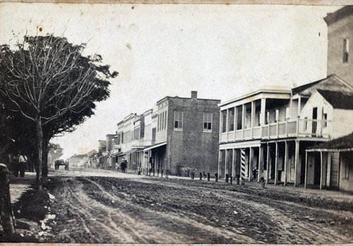 Black and white photograph of buildings lining Elizabeth Street in Brownsville, Texas. Photograph by Louis de Planque, 1865.