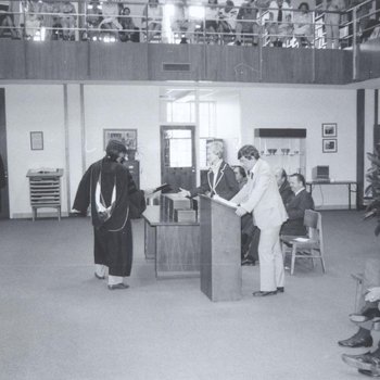 Walter Dellinger stands at lectern during graduation in library reading room.  Charlie Howell, Dean of Admissions, stands on his right.