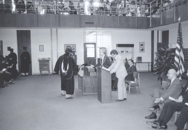 Walter Dellinger stands at lectern during graduation in library reading room.  Charlie Howell, Dean of Admissions, stands on his right.
