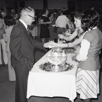 A woman assists a man with the punchbowl on a buffet at an event in the library reading room.