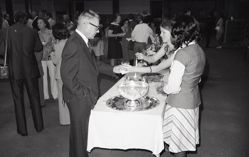 A woman assists a man with the punchbowl on a buffet at an event in the library reading room.