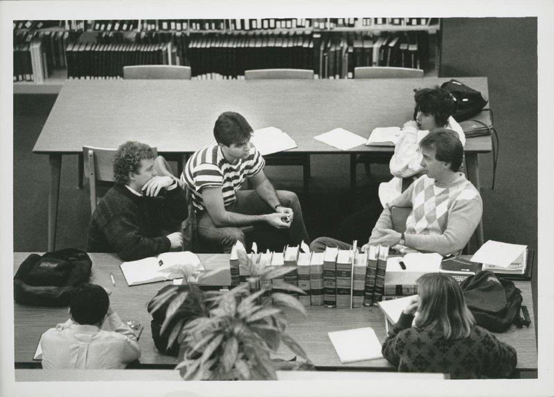 Students sit at tables in library talking.