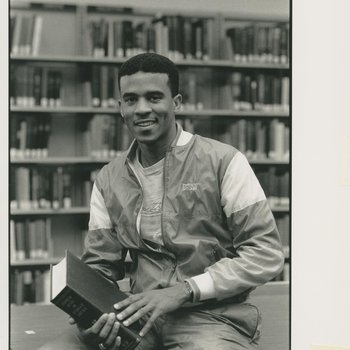 Portrait of Spruell Driver '91 in library sitting on table holding book.