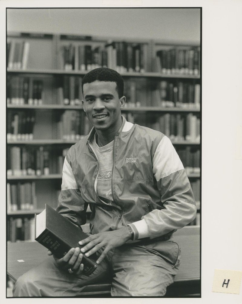 Portrait of Spruell Driver &#x27;91 in library sitting on table holding book.