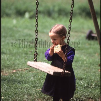 Amish girl eating behind swing