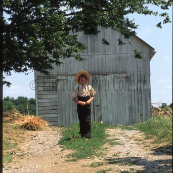 Boy stands in front of white barn