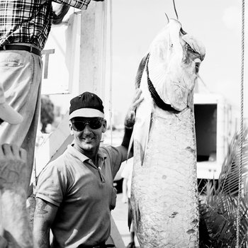 A contestant stands next to tarpon with hand near pectoral fin