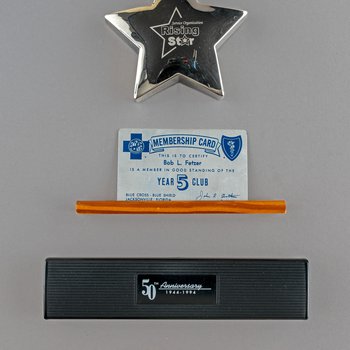Rising Star paperweight, undated; Metal membership card and stand, Bob Fetzer, Blue Cross-Blue Shield 5 Year Club, undated; 50th Anniversary pen and box, 1994