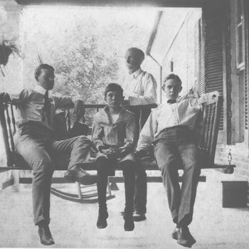 Ward Smith, Frank Kercheval, and George G. Mitchell seated on a porch swing with Charles Mitchell Sr. standing behind them.