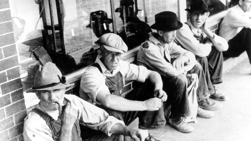 Men sitting against brick building during the Great Depression.