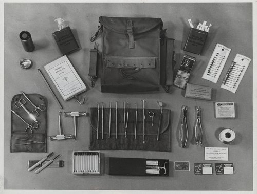 Black and white photo of a WWII dental field kit. Includes leather satchel, metal dental tools, pins, antiseptics, etc.