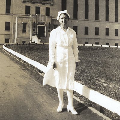 Full body portrait of Marguerite Andell in an all-white nursing uniform and cap.