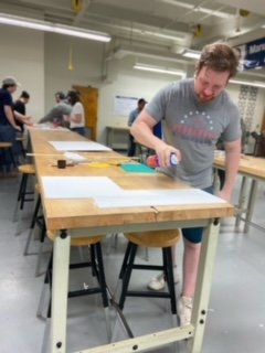 Student Brandyn Hardie spraying adhesive to foam core board