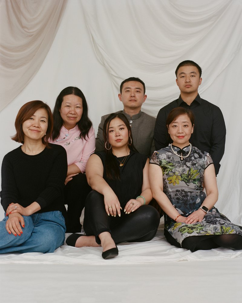 A group of six people with Chinese roots, two men and four women, sitting or kneeling against a white backdrop.