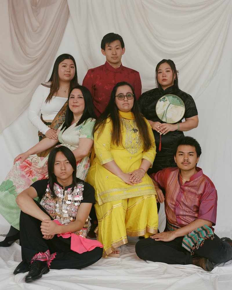 A group of seven people, three men and four women against a white backdrop. All of the people are wearing traditional clothing of Asian countries.