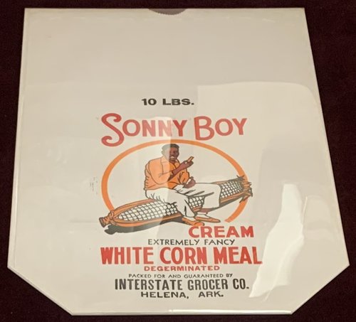 Empty sack from 10-pound package of "Sonny Boy Cream Extremely Fancy White Corn Meal, Degerminated. Packed for and Guaranteed by Interstate Grocer Co., Helena, Ark." Package features an illustrated Sonny Boy Williamson II, holding a harmonica, sitting on a giant ear of white corn.