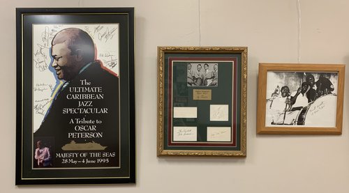 3 framed items hang on the wall: The Ultimate Caribbean Jazz Spectactular: A Tribute to Oscar Peterson (1995); Collected autographs of Buddy Holly and the Crickets; Framed photo of Sonny Boy Williamson with Frank Frost