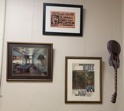 3 framed items hang on the wall: Framed Photo of Pool Hall by Birney Imes; Poster for R&B at the Ricky-Tick Club, Plaza Ballroom, Guildford [1964]; Poster from Charleston Blues Festival, February 14-22, 1992; Guitar embellished by artist Lamar Sorrento