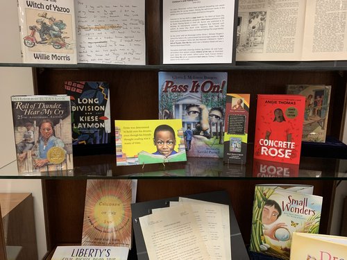 display case containing publications by Mildred D. Taylor, Kiese Laymon, Gloria J. McEwen Burgess, Angie Thomas, and Virginia Fairfax