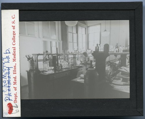 A slide picturing a chemistry laboratory at MUSC from the mid-1900s. "Chemistry Lab," and "62.," handwritten, appear on the label of the slide. "Dept. of Med. Illus., Medical College of S.C.," typed, also appears on the label of the slide.