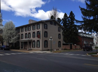 Photograph of large, well-kept, three-story house sitting at corner of two streets, with several trees nearby.
