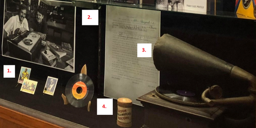 photo of items in display case includes numbers corresponding to list:  trading cards, recording contract, Victrola, wax cylinder