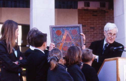 Man at podium holds up stained glass window while children look on