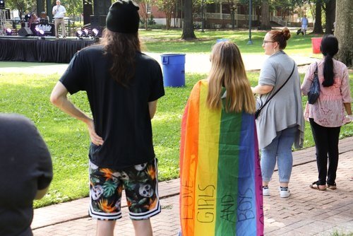 A bystander wears a rainbow flag like a superhero cape (written on flag: I love girls and boys)