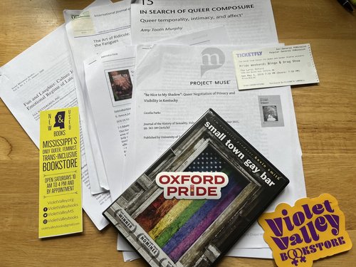 A pile of printed articles, a DVD copy of Small Town Gay Bar, and local stickers
