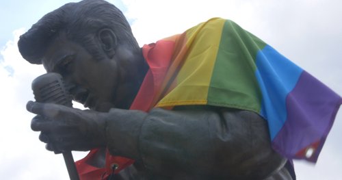 A close up of the face of the Elvis Presley statue wearing the rainbow flag as a cape