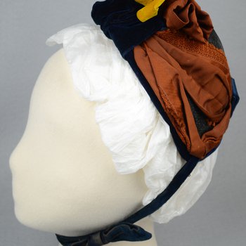 Bonnet, black straw capote trimmed with blue velvet, silk ribbons in blue and dark orange, and artificial flowers, 1880s, side view